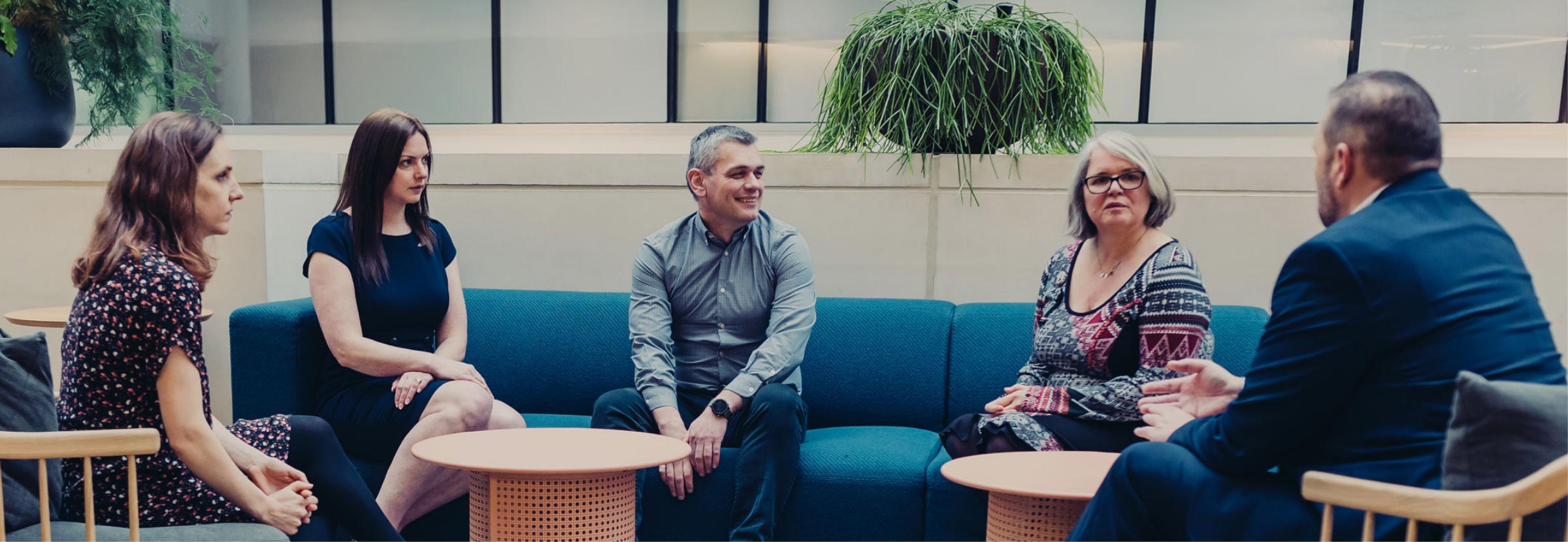 The image portrays a team of professionals from Alderley Analytical, engaged in a discussion in a relaxed, informal setting. The group is seated across from each other on comfortable, modern furniture, fostering a sense of open dialogue and collaboration. The presence of a plant hanging overhead and the natural light from the windows contribute to a warm and inviting atmosphere, emphasizing a work environment that values communication and team cohesion. This scene likely represents a moment of strategic planning, idea sharing, or team building, illustrating the company's commitment to fostering a collaborative and supportive workplace culture. The diverse team, shown in professional attire, reflects a range of roles and expertise within Alderley Analytical, highlighting the multidisciplinary approach the company employs to achieve excellence in bioanalytical services. This image effectively conveys the human element of Alderley Analytical, showcasing the professionals behind the science and their collaborative efforts to drive innovation and maintain high standards in their field.