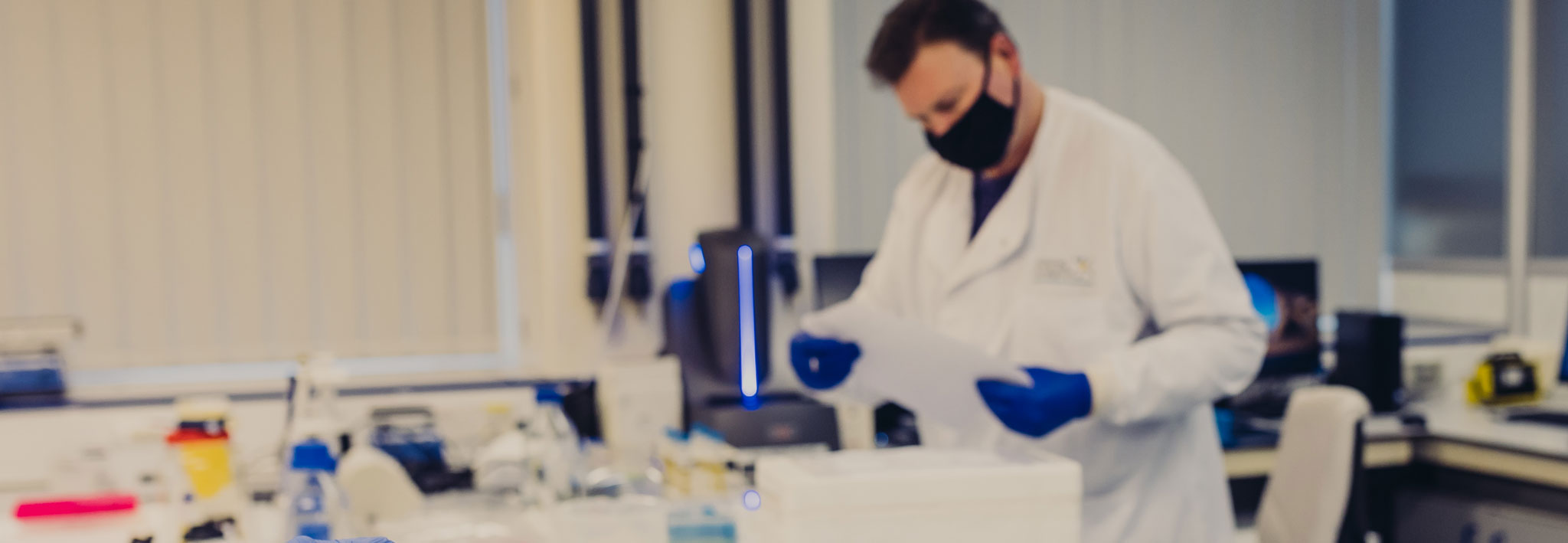 scientist in black mask, white coat and blue gloves in a laboratory